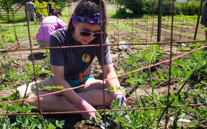 a student wearing gloves sits and works in a garden during a service project with outward bound